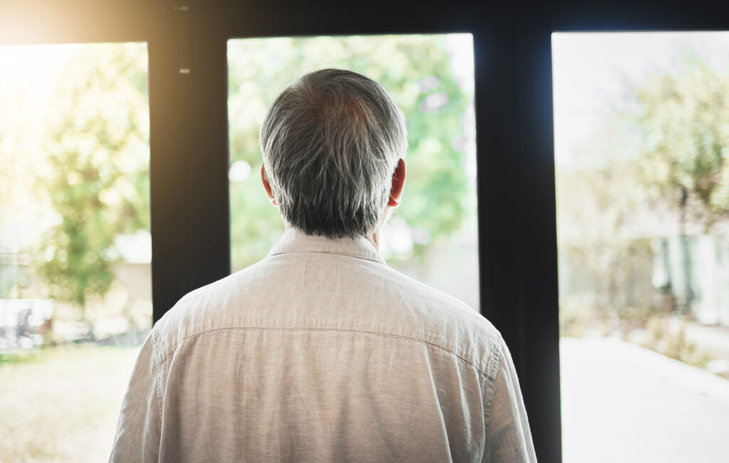mature man and thinking by window, experiencing symptoms of testosterone deficiency including fatigue, weight changes, low libido, and declining drive